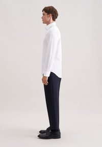 Witte blouse met lange mouwen, slim fit, gecombineerd met marineblauwe broek. De blouse heeft een klassieke kraag en manchetten met knopen. Inclusief zwarte nette schoenen.