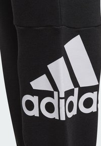 Černé tepláky s výrazným bílým logem Adidas. Vyrobené z měkké látky, design zahrnuje mírně texturovaný povrch a zúžený střih nohavic.