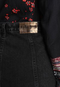 Svarta denimjeans med en guldig etikett som läser "Exotic Jeans by Desigual", tillsammans med en svart blus med blommönster som visar livfulla röda blommor.