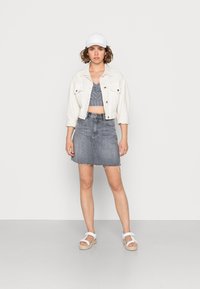 Jaqueta de denim branca, top curto riscado azul, saia de denim cinza com bainha desfiada e sandálias brancas. Design simples com cores neutras.
