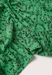 Tissu vert à imprimé floral noir, avec des coutures froncées et élastiquées créant un effet texturé et plissé.