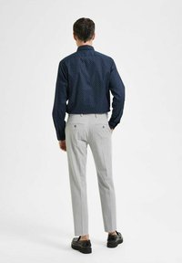 Mornarska majica s belimi pikami, v kombinaciji s svetlo sivo hlačami. Obleka ima ozek kroj in črne čevlje, prikazana s hrbtne strani.