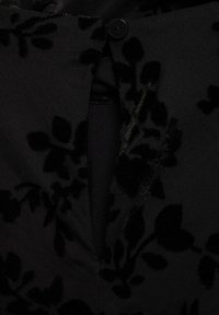 Close-up of black fabric with raised velvet floral pattern and a buttoned slit opening.