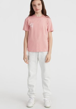 T-shirt en coton rose à manches courtes avec l'imprimé "Women of the Wave". Associé à un pantalon de survêtement gris clair et des baskets blanches.