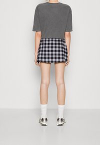 Šedé tričko s krátkým rukávem v kombinaci s tmavomodrou kostkovanou sukní. Modelka má na sobě bílé ponožky a metalické tenisky. Hladká látka s kostkovaným vzorem.