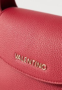 Czerwona skórzana torebka o fakturowanej powierzchni z złotym logo "VALENTINO" na przodzie. Charakteryzuje się zgrabnym kształtem i minimalistycznymi elementami metalowymi.