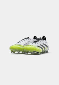 Scarpe da calcio grigie con accenti gialli vivaci, tomaia testurizzata, lacci neri e tacchetti trasparenti su una suola a profilo basso.