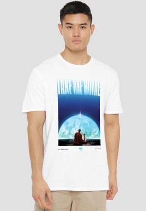 Man wearing white t-shirt with graphic showing Superman and dog sitting on a ledge looking at Earth with the text "Take Me Home."