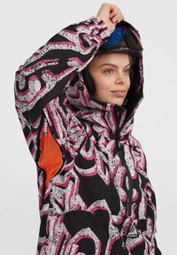Zwarte sneeuwjas met roze abstracte patronen, capuchon en geventileerde zijzakken met oranje gaasvoering. Verstelbare manchetten en zichtbare merkdetails.