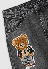 Tessuto denim nero con una patch a forma di orso, caratterizzata da pelliccia color crema, paillettes e dettagli ricamati, accentuata da un motivo nero e colorato sull'abbigliamento.