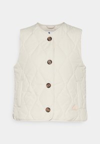 Přešívaná béžová vesta s kulatým výstřihem, čtyřmi hnědými knoflíky a bočními kapsami. Na spodním pravém rohu obsahuje malou logovou nášivku.