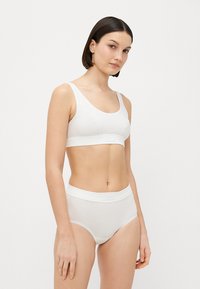 Bijeli pamučni bralet i gaće visokog struka. Glatka tekstura, bezšavni dizajn, široke naramenice i elastične gumice. Minimalistički stil.
