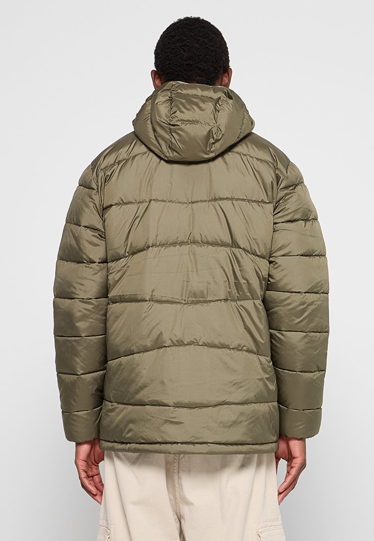 Chaqueta acolchada verde oliva con capucha, con un diseño acolchado y puños elásticos. La textura es suave y el brillo refleja la luz de forma sutil.