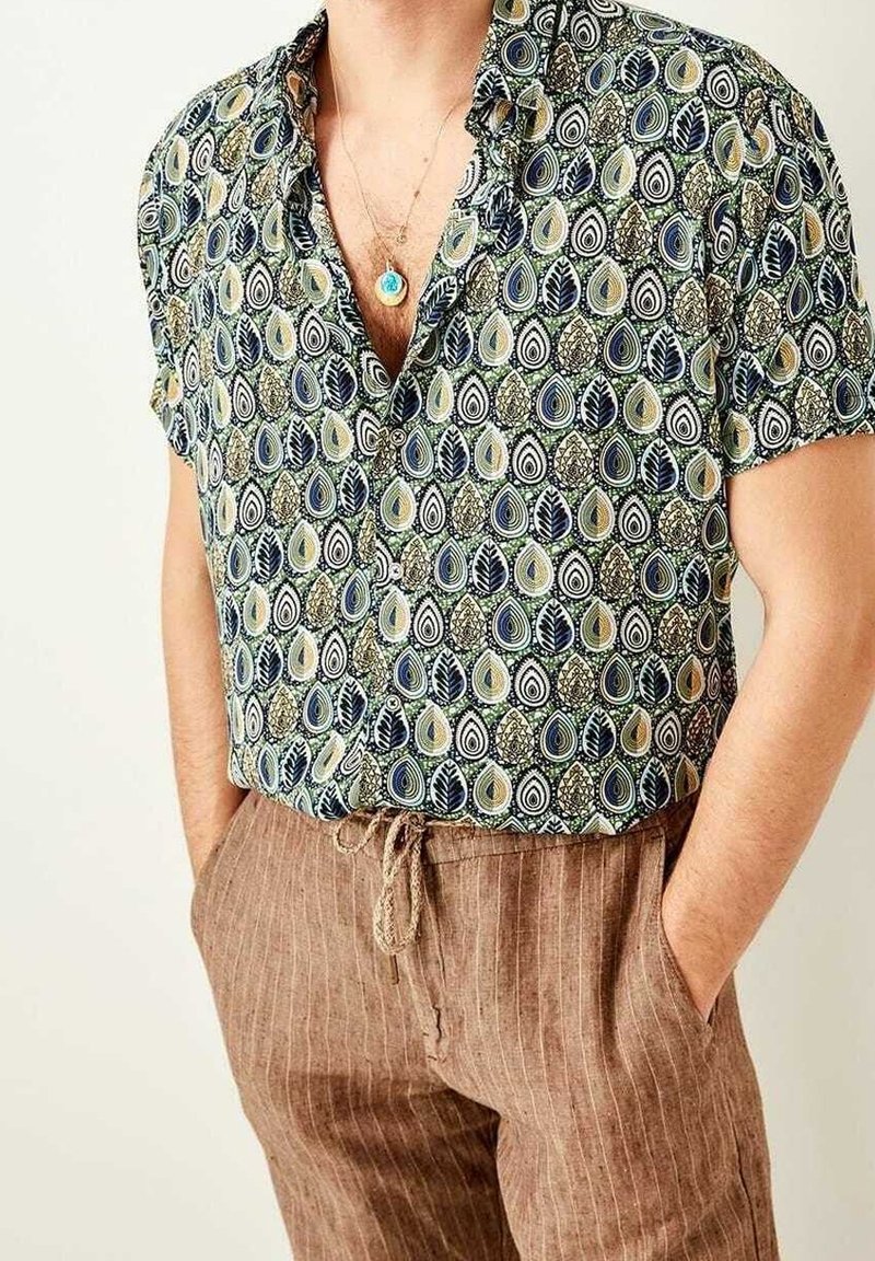 Kurzarmhemd in Grün, Marineblau und Creme mit einem Blatt- und Tränenmuster; kombiniert mit braunen gestreiften Jogginghosen mit Kordelzug.