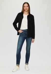 Black button-up shirt over a white t-shirt, paired with blue skinny jeans and white sneakers. Smooth fabric, fitted design, rolled cuffs.