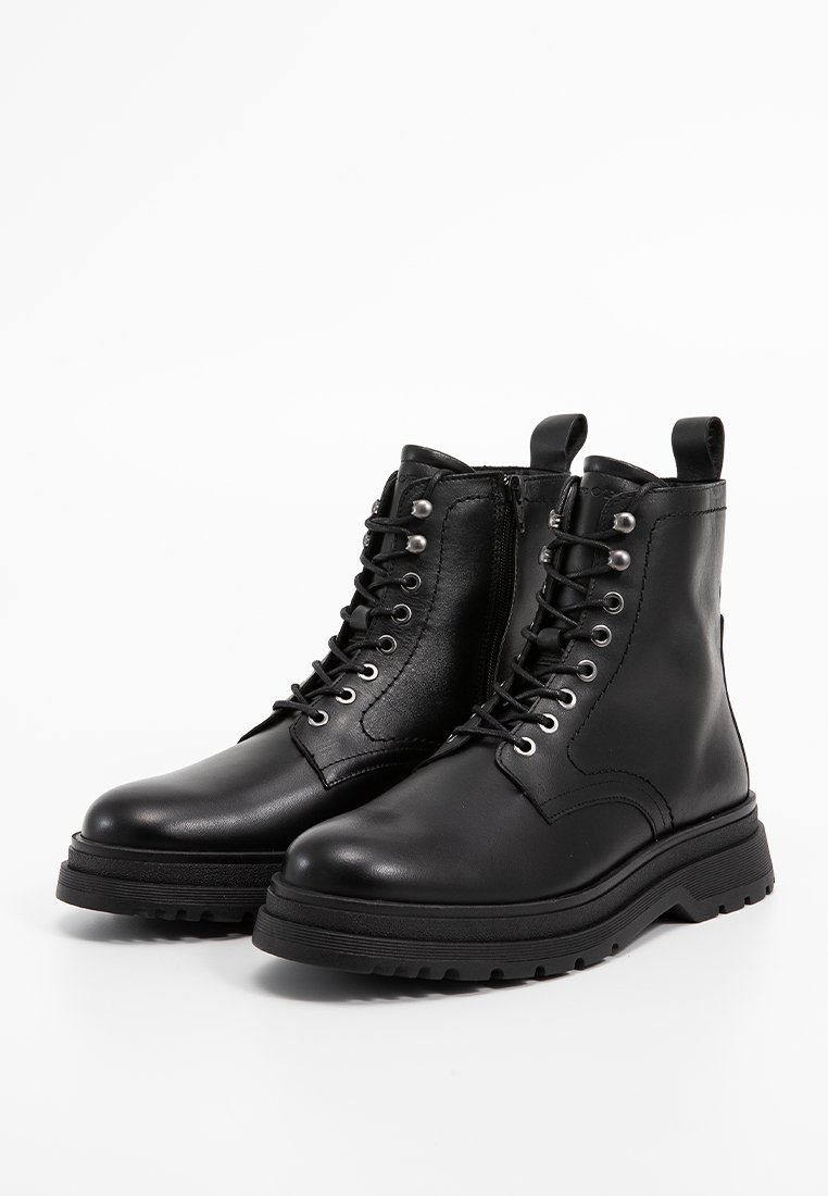 Schwarze Lederstiefeletten mit runden Zehen, dicken Gummisohlen, Metallösen und Schnürsenkeln, ausgestattet mit einer Schlaufe auf der Rückseite für leichtes Anziehen.