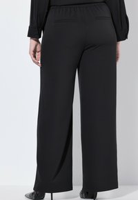 Svarta vida byxor med elastisk midja. Slät tygkvalitet med en minimalistisk design och två bakfickor, som erbjuder en avslappnad passform.