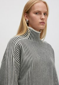 Schwarz-weißer gestreifter Rollkragenpullover mit gerippter Textur und hohem Kragen, der überdimensionale Schultern und eine lockere Passform aufweist.