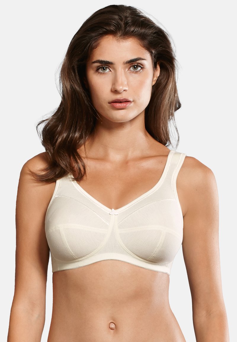 Soutien-gorge beige avec de larges bretelles, tissu à texture douce et détails de coutures. Présente un accent nœud central et un design couvrant.