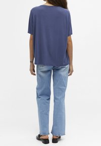 T-shirt blu navy a manica corta con vestibilità rilassata, realizzato in tessuto morbido, abbinato a jeans dritti azzurri e scarpe con slip-on nere.