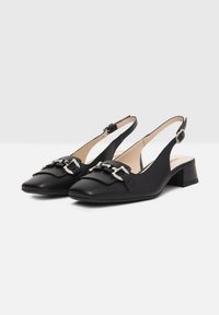 Zapatos de slingback de cuero negro con un bajo tacón bloque, detalles decorativos de hebilla y un diseño de punta redonda. Textura suave en toda su superficie.
