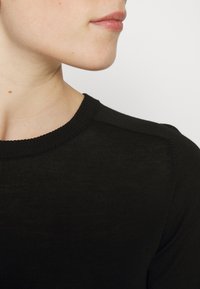 Black knit sweater with a round neckline, made from a lightweight material, featuring a smooth texture and reinforced shoulder seams.