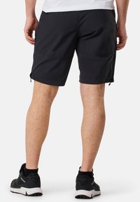 Schwarze Shorts aus leichtem Material, mit seitlichen Taschen, einem flachen Bund und einem knielangen Schnitt. Getragen mit schwarzen Sportschuhen.