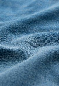 Tejido de mezclilla en azul claro, con una textura suave y patrones de tejido sutiles, exhibido en pliegues y curvas suaves.