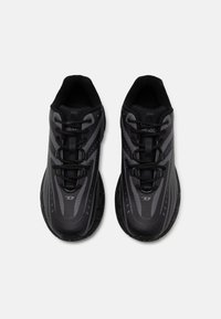 Baskets de sport noires au design épuré, avec un dessus texturé, des rayures grises contrastées et des lacets noirs. Semelle rigide en caoutchouc.