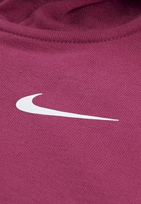 Burgunderfarbener Stoff mit glatter Textur zeigt ein weißes Nike-Swoosh-Logo. Der Nahaufnahmewinkel hebt die Nähte und Webdetails hervor.