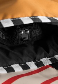 Intérieur multicolore d'un sac affichant un tissu à rayures noires et blanches, des accents orange et une sangle noire texturée avec un bouton-pression argenté.