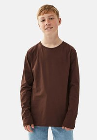 Ruskohalon pitkähihaisen paidan valmistettu puuvillasta, jossa on pyöreä kaula-aukko ja rento istuvuus, yhdistettynä vaaleansinisiin farkkuihin.