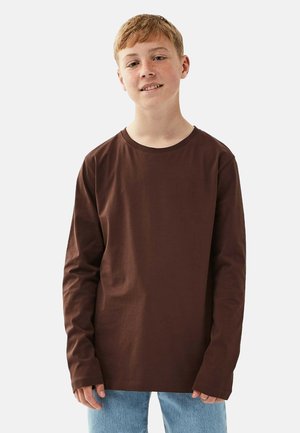 Braunes Langarm-T-Shirt aus Baumwolle, mit rundem Ausschnitt und lässiger Passform, kombiniert mit hellblauen Jeans.