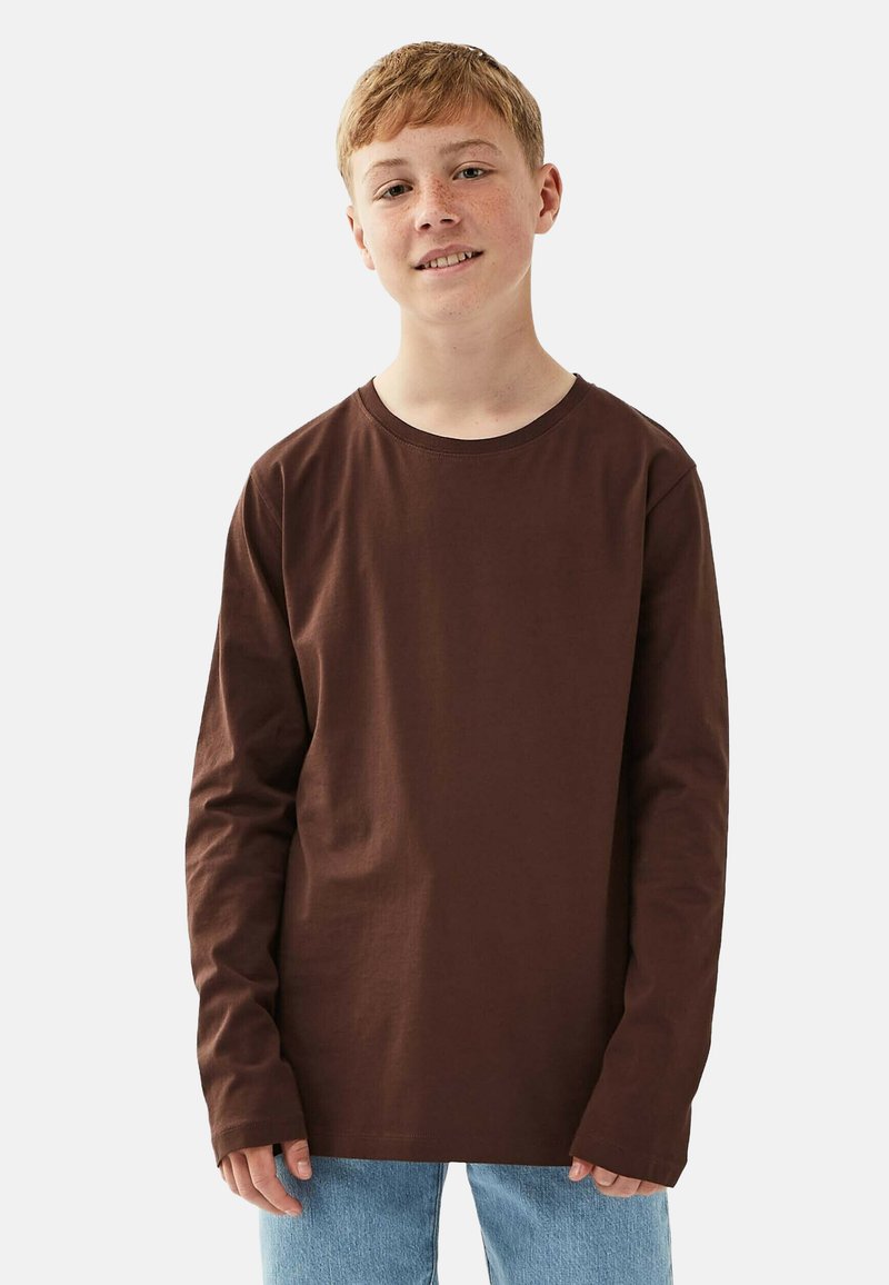 Ruskohalon pitkähihaisen paidan valmistettu puuvillasta, jossa on pyöreä kaula-aukko ja rento istuvuus, yhdistettynä vaaleansinisiin farkkuihin.