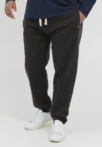 Sorte joggebukser med elastisk midje og kremfarget snor, sidelommer og smalere ben. Kombinert med hvite sportssko.