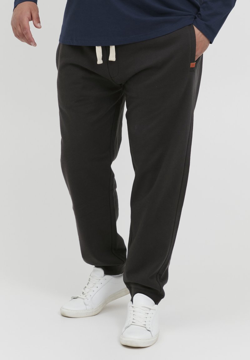 Sorte joggebukser med elastisk midje og kremfarget snor, sidelommer og smalere ben. Kombinert med hvite sportssko.