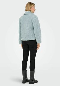 Light blue, textured, fuzzy jacket with a collar and long sleeves, paired with black pants and ankle boots. View shows the back.