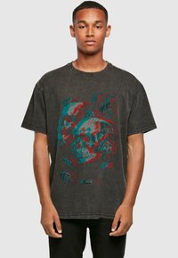 Sort bomulds T-shirt med et grafisk design af overlappende kranier i rød og teal. Slidte kanter tilføjer tekstur til den afslappede pasform.