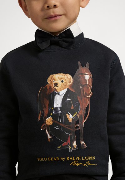 Svart sweatshirt med en bjørn i formell bekledning ved siden av en hest. Bjørnen har på seg smoking, sløyfe og har detaljert pelsstruktur.