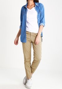 Denim button-up shirt, white graphic t-shirt, khaki chinos, white sneakers. Casual outfit with layered textures and neutral color palette.