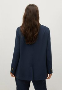 Blazer entallado azul marino hecho de tela suave, con una sola abertura en la parte posterior, mangas largas y detalles de puños con botones.