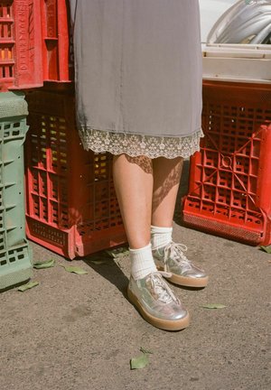Sneakers piattaforma argento con texture liscia, calzini bianchi a coste e un vestito grigio con bordi in pizzo; posizionati vicino a casse colorate.