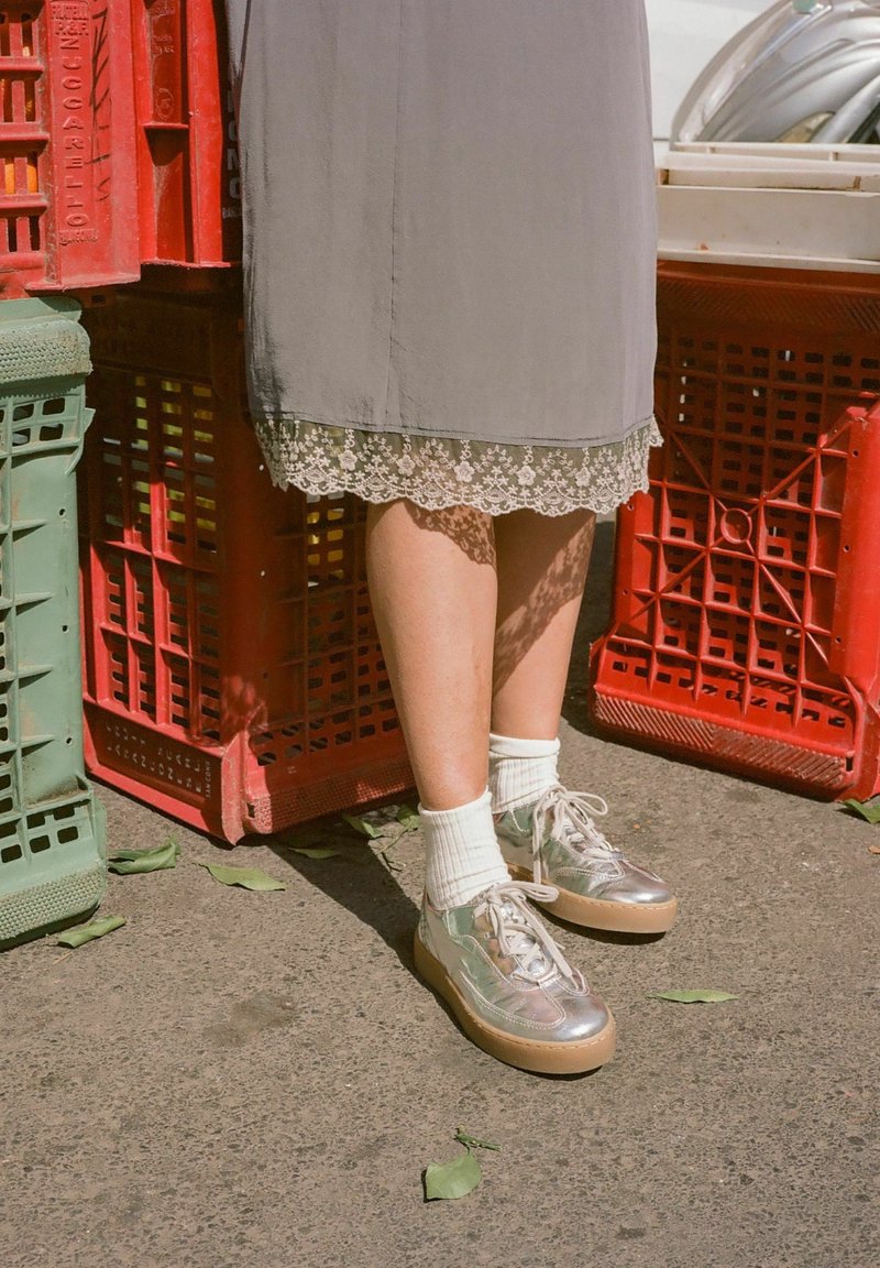 Sneakers piattaforma argento con texture liscia, calzini bianchi a coste e un vestito grigio con bordi in pizzo; posizionati vicino a casse colorate.