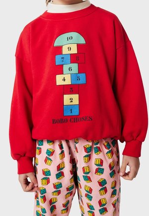 Barn iført rød sweatshirt med hinkerude nummereret 1-10 og flerfarvede bukser med terningemønster på lys baggrund.