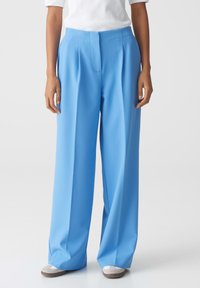 Lichtblauwe wijde broek gemaakt van een gladde stof, met een voornaad en een op maat gemaakte tailleband. Gecombineerd met neutraal gekleurde schoenen.