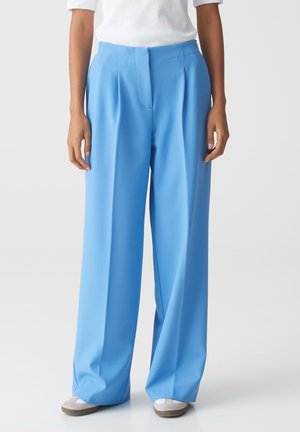 Lichtblauwe wijde broek gemaakt van een gladde stof, met een voornaad en een op maat gemaakte tailleband. Gecombineerd met neutraal gekleurde schoenen.