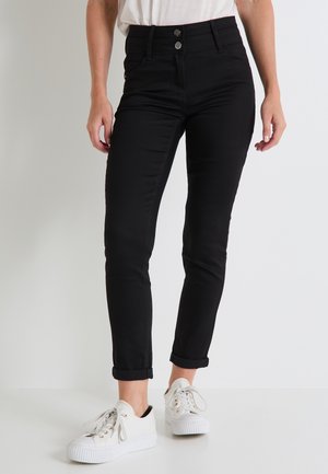 Jeans negros de cintura alta con un ajuste ceñido, dos botones frontales, dobladillos enrollados y una textura suave, combinados con zapatillas blancas.