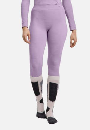 Person iført lavendelleggings og lange sokker med sorte og beige geometriske mønstre, stående mod en ensfarvet baggrund.