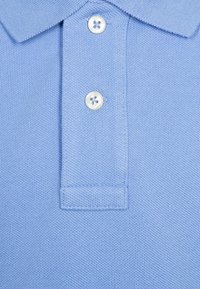 Ljusblå pikétröja med en texturerad tygkonstruktion, treknapps avslutning och klassisk kragsdesign.