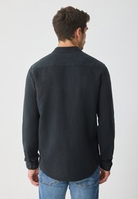 Dunkles Langarmhemd aus weichem Stoff, mit klassischem Kragen, geknöpften Manschetten und abgerundetem Saum, kombiniert mit blauen Jeans.